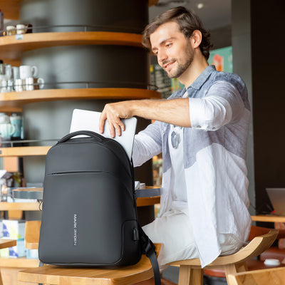 Man in cafe with Mark Ryden Limit anti-theft usb charging backpack. 